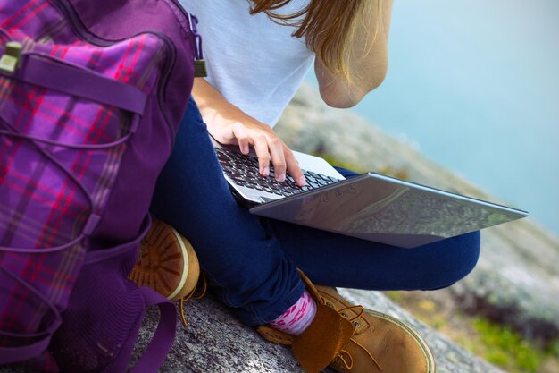 Randonneuse avec un ordinateur portable assis sur un rocher sur fond de montagnes et de lacs