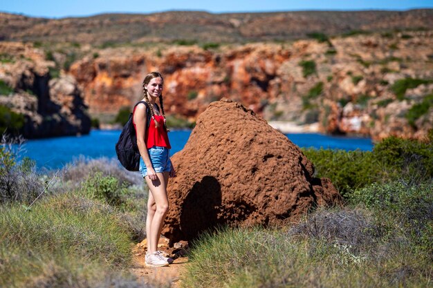 une randonneuse avec un sac à dos se tient près d'une grande termitière au-dessus d'une gorge dans l'ouest de l'australie