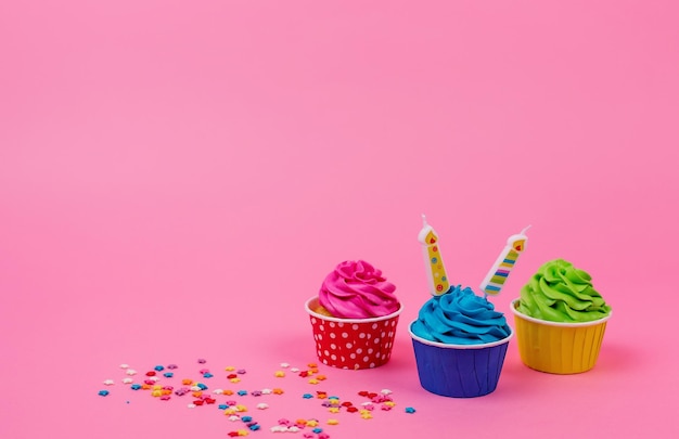 Une rangée de cupcakes colorés avec des bougies sur fond rose