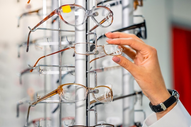 Rangée de lunettes chez un opticien Boutique de lunettes Stand avec lunettes dans le magasin d'optique Vitrine avec lunettes dans un magasin ophtalmique moderne Main choisissant des lunettes Gros plan