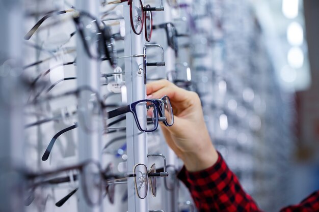 Rangée de lunettes chez un opticien. Boutique de lunettes. Tenez-vous avec des lunettes dans le magasin d'optique. La main de la femme montre des lunettes