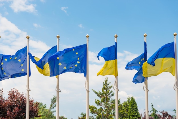 Rangée de mâts avec des drapeaux de l'Union européenne et de l'Ukraine flottant au vent sur fond de ciel bleu