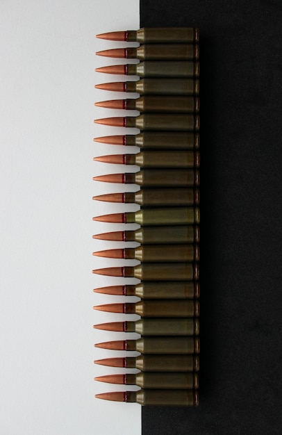 Rangée de munitions réelles, à moitié allongées sur une surface noire et à moitié sur une photo verticale à surface blanche