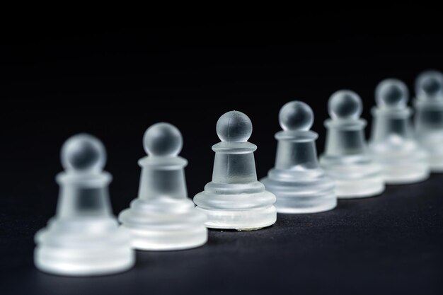 Rangée de pions d'échecs en verre opaque sur fond noir gros plan de mise au point sélective