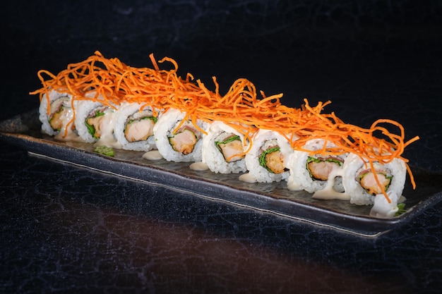 Une rangée de sushi maki avec du saumon décoré de carottes hachées servies sur une assiette en marbre placée sur une table noire