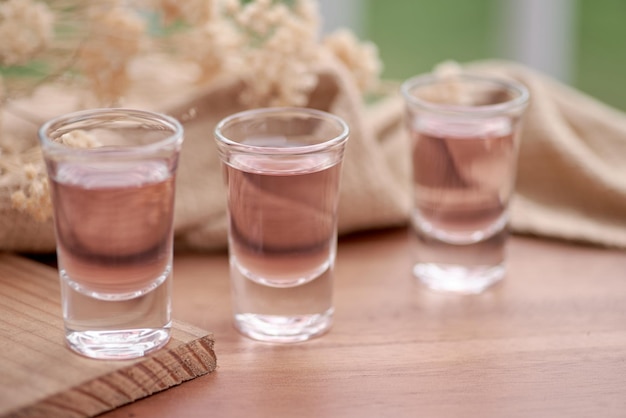 Une rangée de verres à liqueur avec un liquide rose sur un dessous de verre