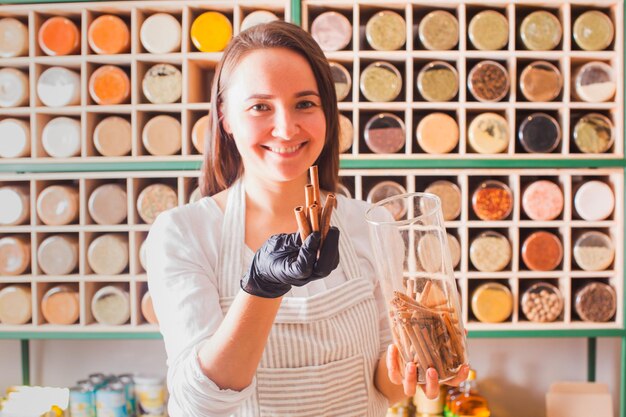 Des rangées droites de verres avec diverses herbes grimaçantes dans l'épicerie. La femme montre les bâtons de cannelle pour le client