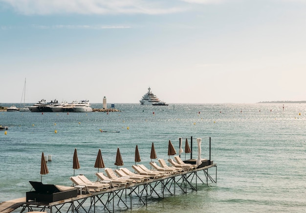 Des rangées de salons de plage vides à Juan les Pins France avec des super yachts en arrière-plan