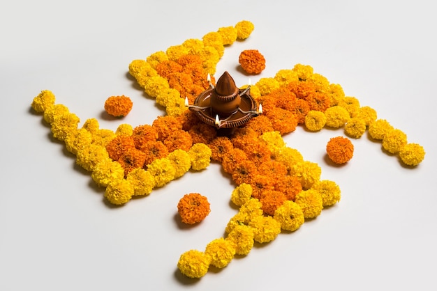 Rangoli de fleurs pour Diwali ou Pongal à base de fleurs de souci ou de zendu et de pétales de rose rouge sur fond blanc avec une lampe à huile en argile au milieu, mise au point sélective