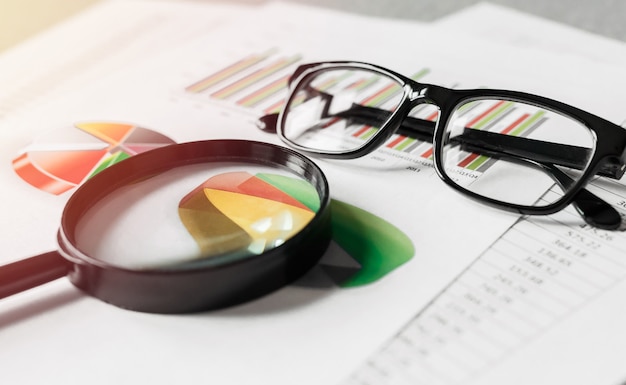 Rapports d'activité et une loupe avec des lunettes sur le bureau de table. Concept d'analyse de données, planification des investissements, analyse commerciale.