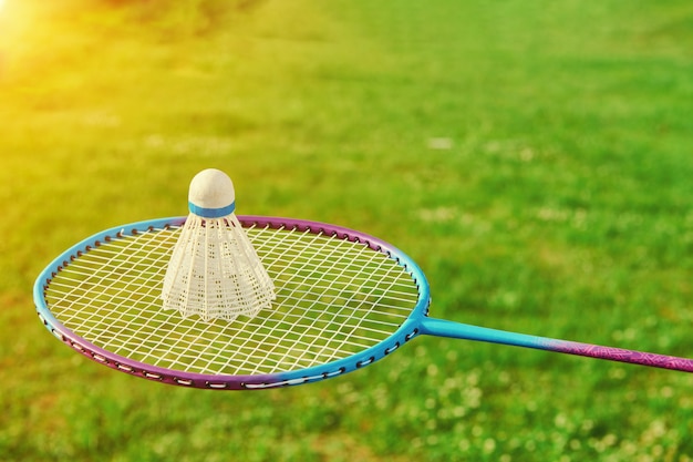 Raquette de badminton avec volant et herbe verte. Activité de jeu de badminton en plein air. Jouer au sport de plein air de badminton. Vue rapprochée avec espace de copie.