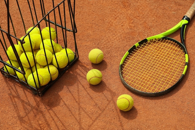 Raquette et panier avec des balles de tennis sur terre battue