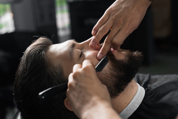 Rasoir droit coupe la barbe de l'homme dans le salon de coiffure. Homme de coiffeur faisant la coiffure pour bel homme.