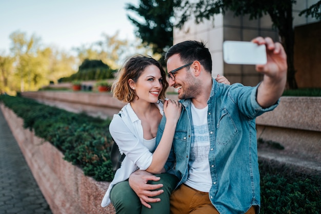 Rassembler les moments lumineux. Souriant jeune couple faisant selfie assis à l&#39;extérieur.