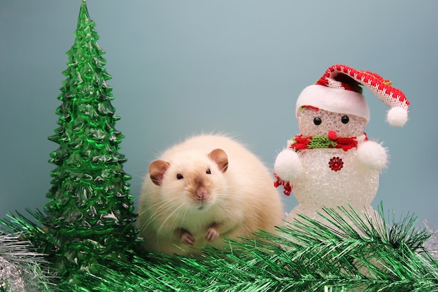 Un rat près d'un arbre de Noël en jouet et d'un bonhomme de neige parmi des guirlandes.