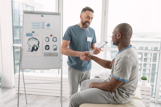 Ravi de vous rencontrer. Joyeux médecin positif souriant tout en serrant la main de ses patients