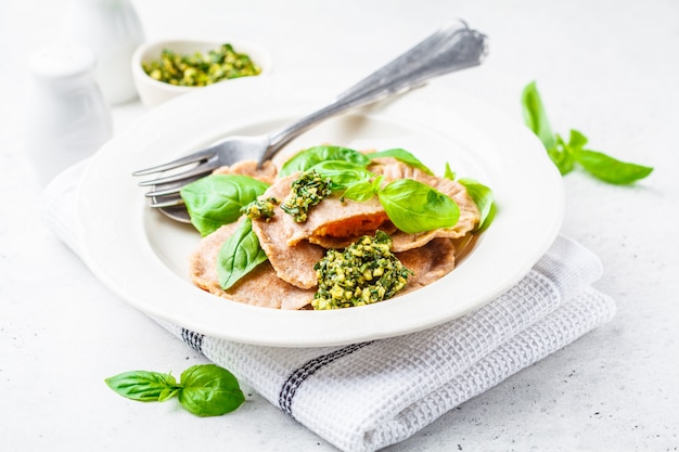 Ravioli à la citrouille avec sauce pesto dans une assiette blanche.