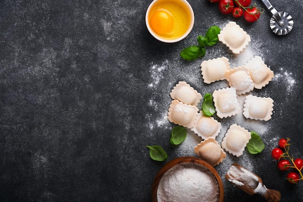 Ravioli Cuisine italienne Savoureuse maison avec de la farine, des tomates, des œufs et des légumes verts sur fond sombre Ingrédients de cuisine alimentaire Fond Vue de dessus