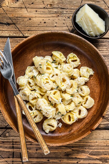 Ravioli ou pâtes tortellini en sauce au fromage à la crème avec de la viande sur table en bois. Vue de dessus.