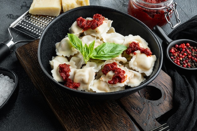 Raviolis appétissants à la sauce tomate, fromage et basilic avec basilic parmesan et tomate dans un bol noir, sur tableau gris