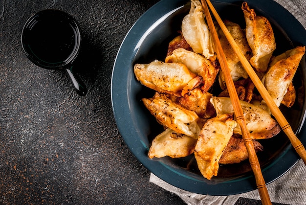 Raviolis asiatiques frits Gyoza sur plaque sombre servi avec des baguettes et de la sauce de soja