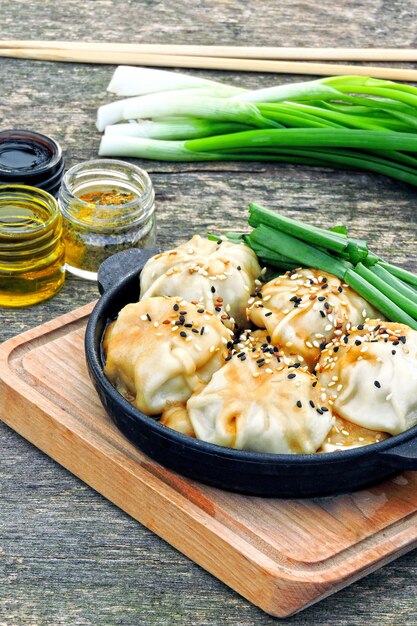 Raviolis chinois à la sauce soja, oignons verts et sésame dans une poêle en fonte. Boulettes dans le style chinois dans une plaque chauffante.