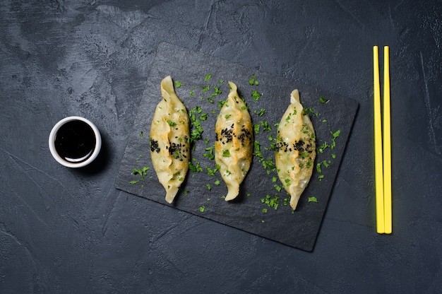 Raviolis coréens frits sur un plateau en pierre noire, baguettes jaunes.