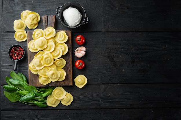 Raviolis crus à la ricotta et aux épinards, sur une planche à découper en bois, sur une table en bois noir, vue de dessus à plat