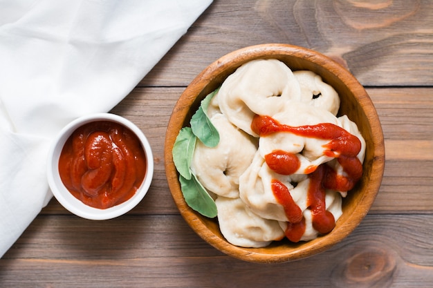 Raviolis cuits saupoudrés de ketchup et de feuilles de roquette dans une assiette en bois