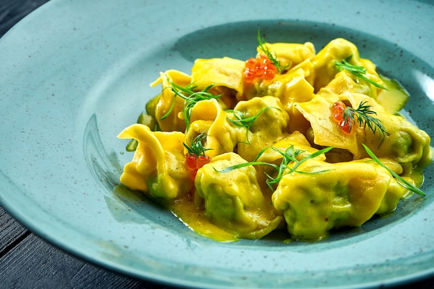 Raviolis faits maison et appétissants au saumon et au caviar, servis avec une sauce à la crème dans une assiette bleue sur une surface en bois sombre. Plat de cuisine italienne