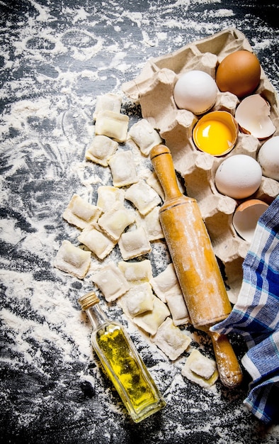 Raviolis frais avec un rouleau à pâtisserie, des œufs et de l'huile d'olive.