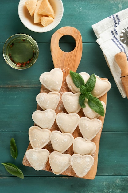 Des raviolis italiens en forme de cœur Des raviolis crus délicieux avec de la farine et du basilic sur un vieux fond bleu en bois Ingrédients de cuisine Arrière-plan Valentines Idées de déjeuner pour la fête des mères Espace de copie en vue supérieure