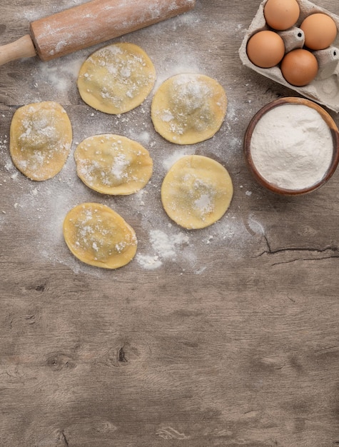 Raviolis ou raviolis farcis non cuits avec de la farine et des ingrédients sur une table en bois avec espace de copie