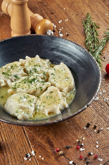 Raviolis ukrainiens bouillis au beurre avec de la viande décorée de légumes verts et de crème sure dans un bol noir sur un savoureux varenyky traditionnel