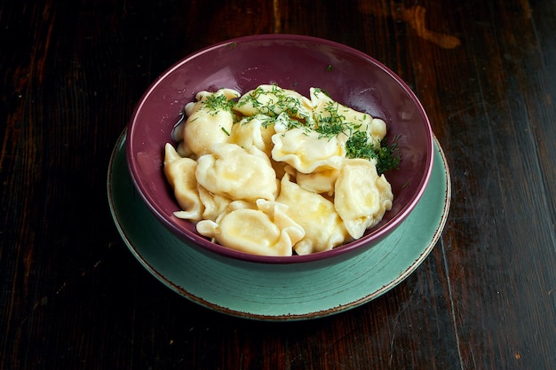 Raviolis ukrainiens traditionnels remplis de coottage salé, servis dans un bol rouge sur fond noir