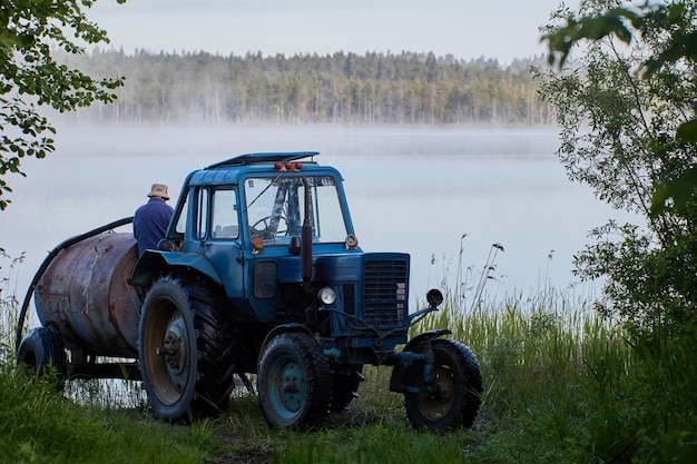 Le ravitaillement en carburant du réservoir du tracteur avec de l'eau du lac forestier tôt le matin avec du brouillard