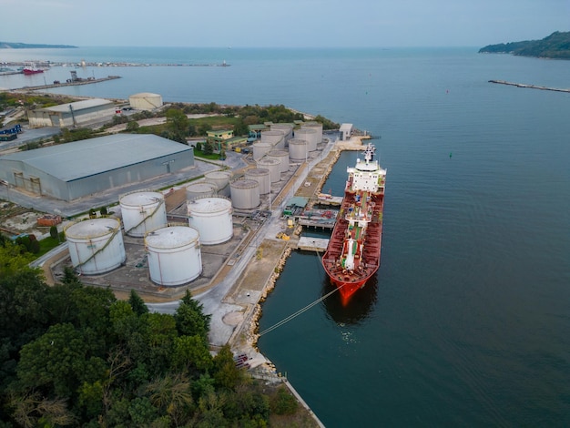 Ravitaillement d'un navire-citerne dans un terminal pétrolier avec silos de stockage dans le port, vue aérienne depuis un drone volant