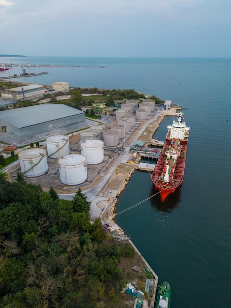 Ravitaillement d'un navire-citerne dans un terminal pétrolier avec silos de stockage dans le port, vue aérienne depuis un drone volant