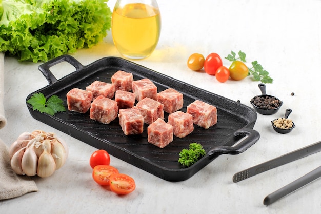 Raw Saikoro Wagyu Cubes Steak de boeuf sur une assiette de steak avec de la laitue à l'arrière-plan, au-dessus du tableau blanc avec d'autres épices à l'arrière-plan