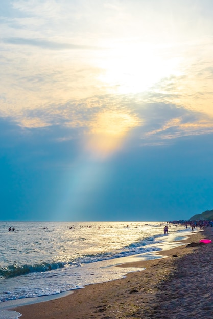 Un rayon de soleil illumine le ciel avec des nuages en orange et une plage de mer d'été avec des touristes