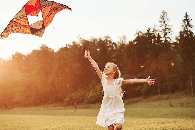 Rayons de soleil incroyables. Une fille heureuse en vêtements blancs s'amuse avec un cerf-volant sur le terrain. Belle nature.