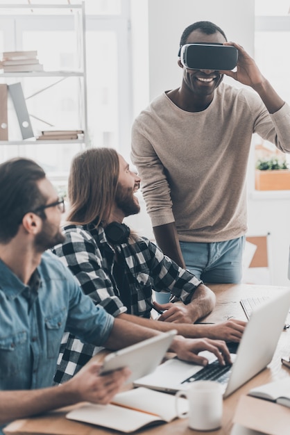 Photo réalité différente. équipe de développement coopérant dans leur bureau tandis que le beau jeune homme ajustant le casque vr et souriant