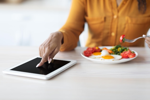 Recadrée de dame noire à l'aide d'une tablette numérique pendant le petit déjeuner