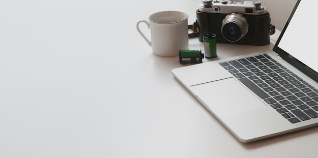 Recadrée de l'espace de travail minimal avec un ordinateur portable et un appareil photo sur une table blanche