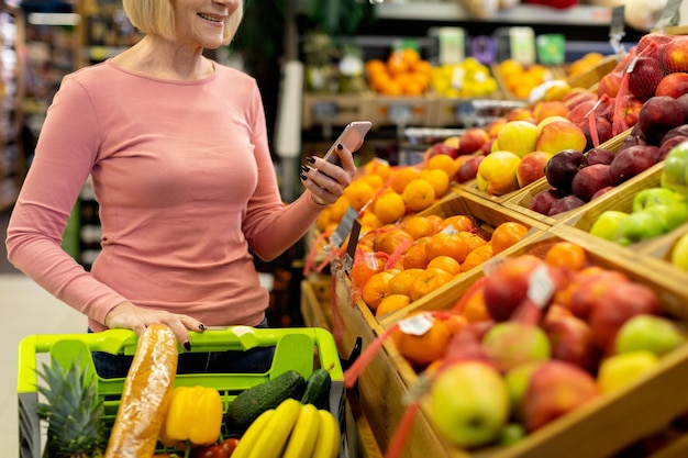 Recadrée d'une femme âgée utilisant un smartphone lors de ses achats au supermarché