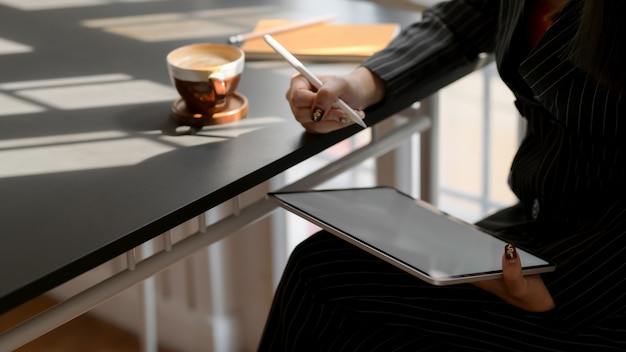 Recadrée de femmes d'affaires écrivant sur une tablette numérique dans un espace de travail confortable