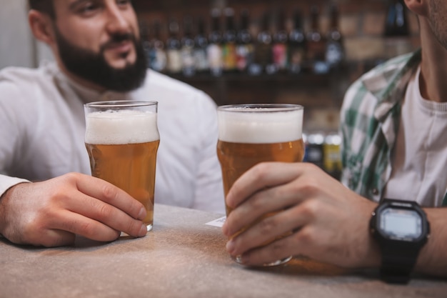 Recadrée gros plan de verres à bière amis masculins tiennent tout en discutant au bar