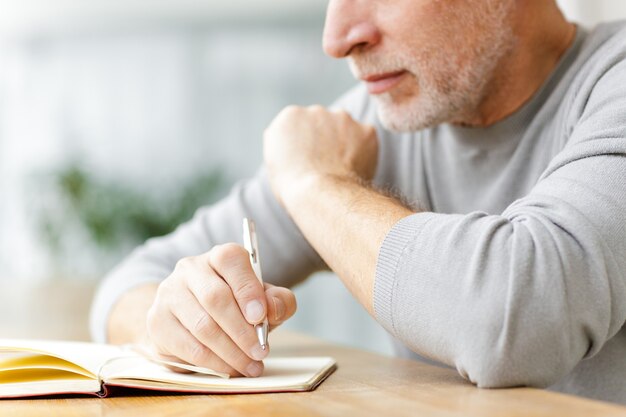 Recadrée un homme d'affaires senior mature s'asseoir dans un café en écrivant des notes dans un cahier.