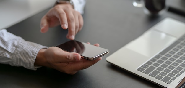 Recadrée de jeune homme d'affaires professionnel à l'aide de smartphone dans son bureau moderne