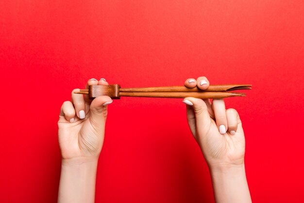 Recadrer l'image de deux mains féminines tenant des baguettes sur fond rouge. Concept prêt à manger avec espace copie